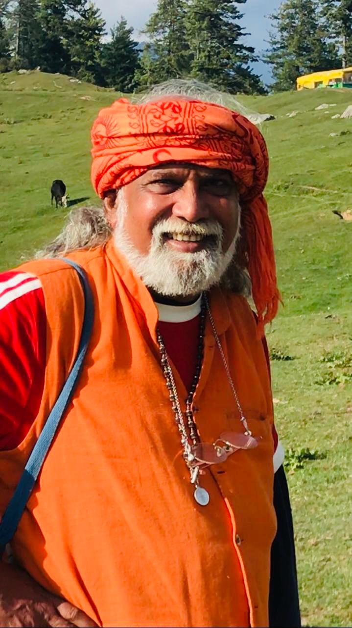 Jyothi Ananda, de turbante e colete laranja, num prado de montanha
